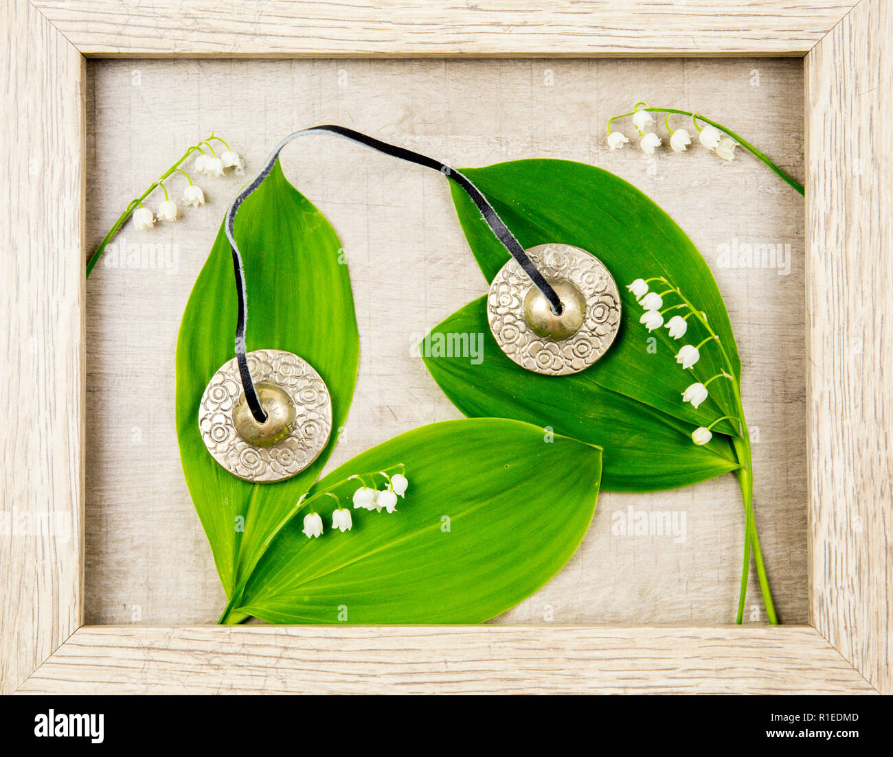 Spiritual silver Tibetan bells on wooden background with white spring flowers Lily of the valley. Stock Photo