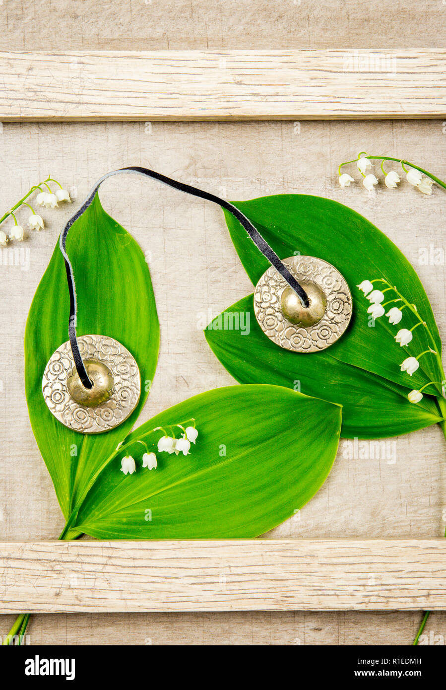 Spiritual silver Tibetan bells on wooden background with white spring flowers Lily of the valley. Stock Photo