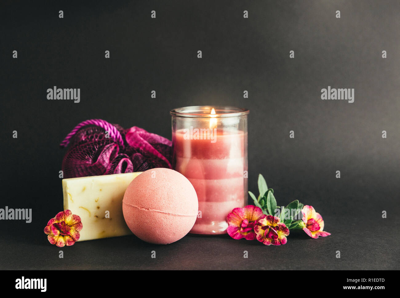Wellness spa therapy pampering products on black background, pink candle burning, warm mood. Pink bath bomb, hand made soap, pink sponge, pink burning Stock Photo
