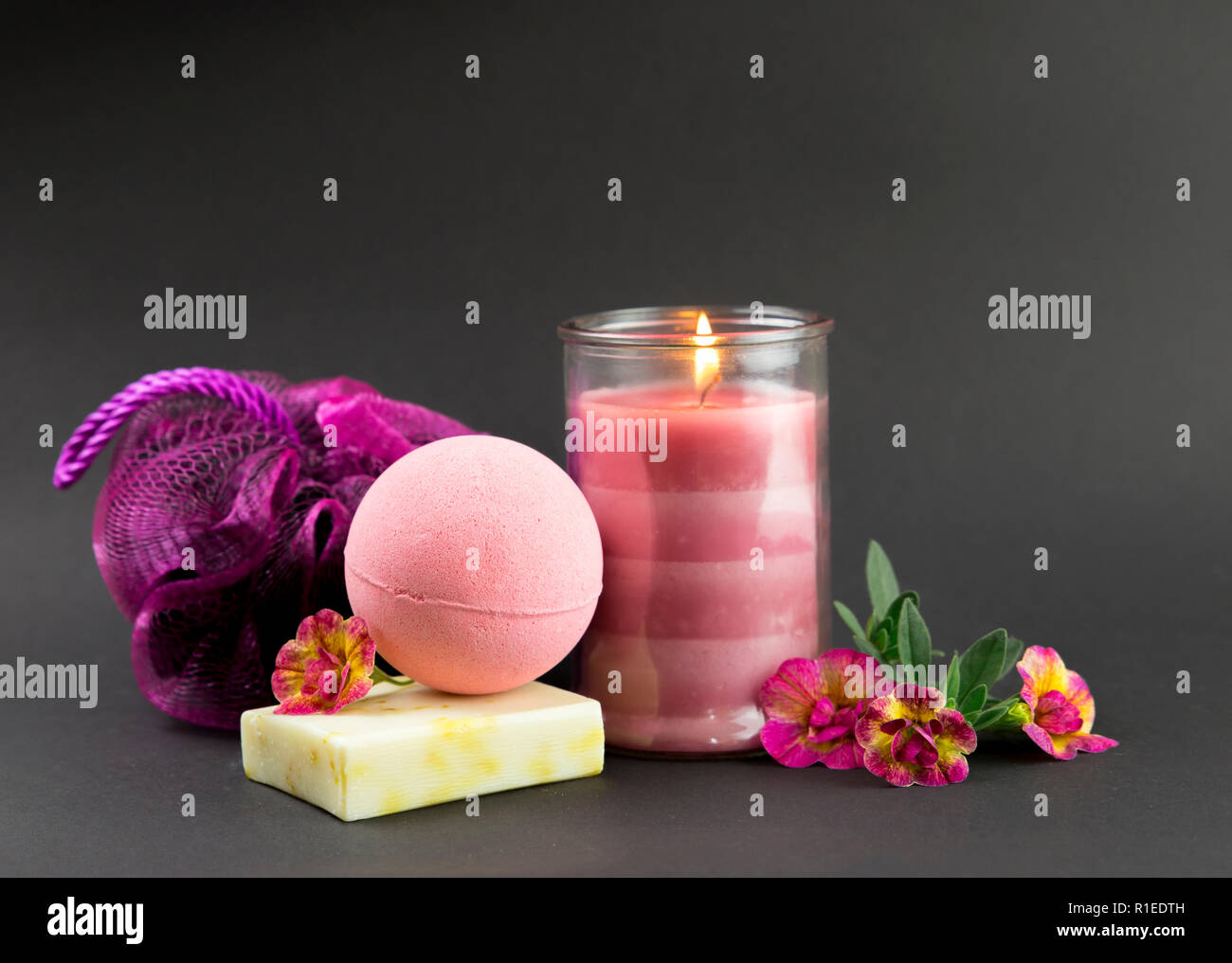 Wellness spa therapy pampering products on black background, pink candle burning, warm mood. Pink bath bomb, hand made soap, pink sponge, pink burning Stock Photo