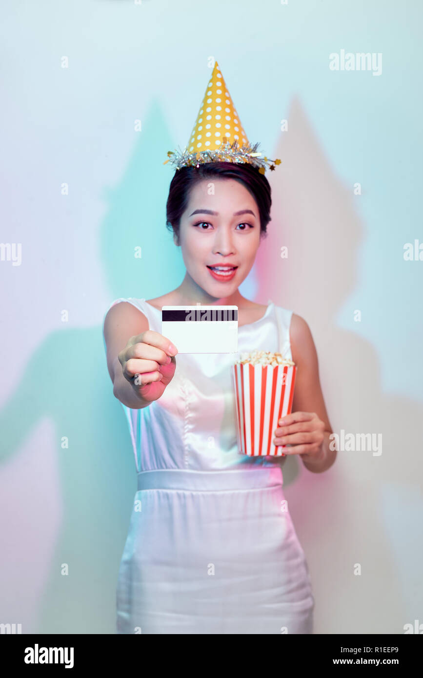 Portrait of young smiling attractive brunette woman in casual clothes watching movie film, holding bucket of popcorn and credit card isolated on white Stock Photo