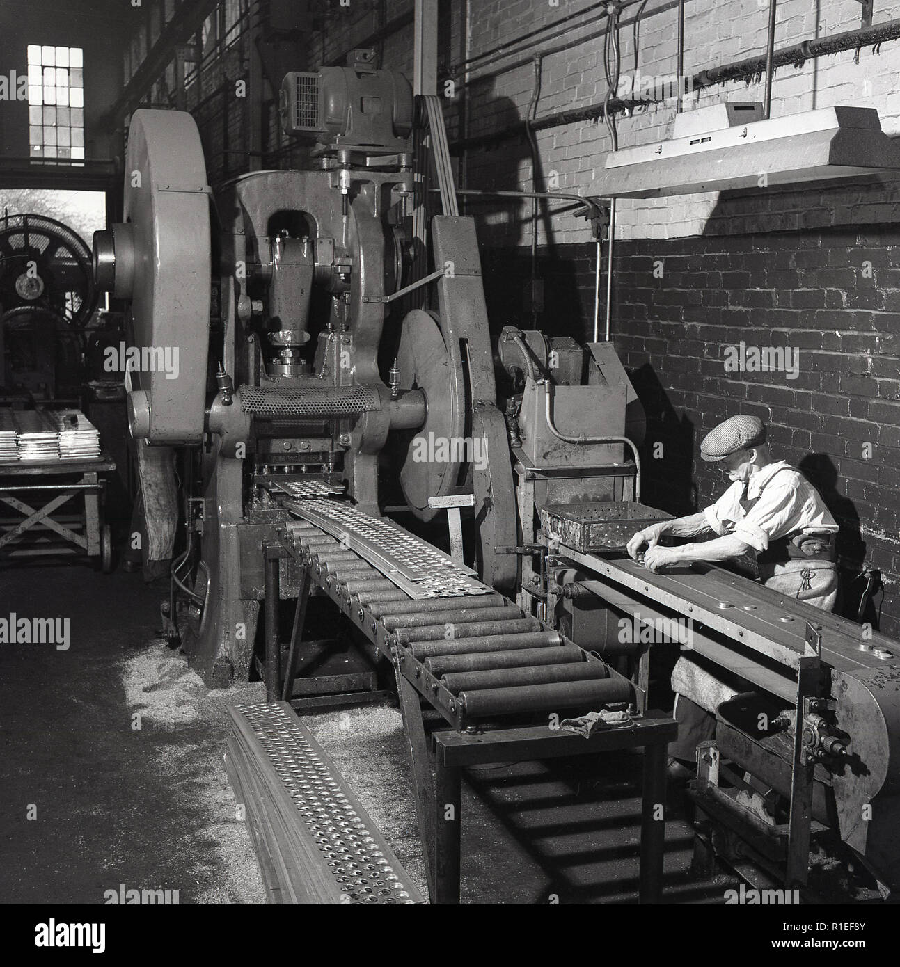 1950s, historical, a male worker wearing a flat cap sitting at a ...