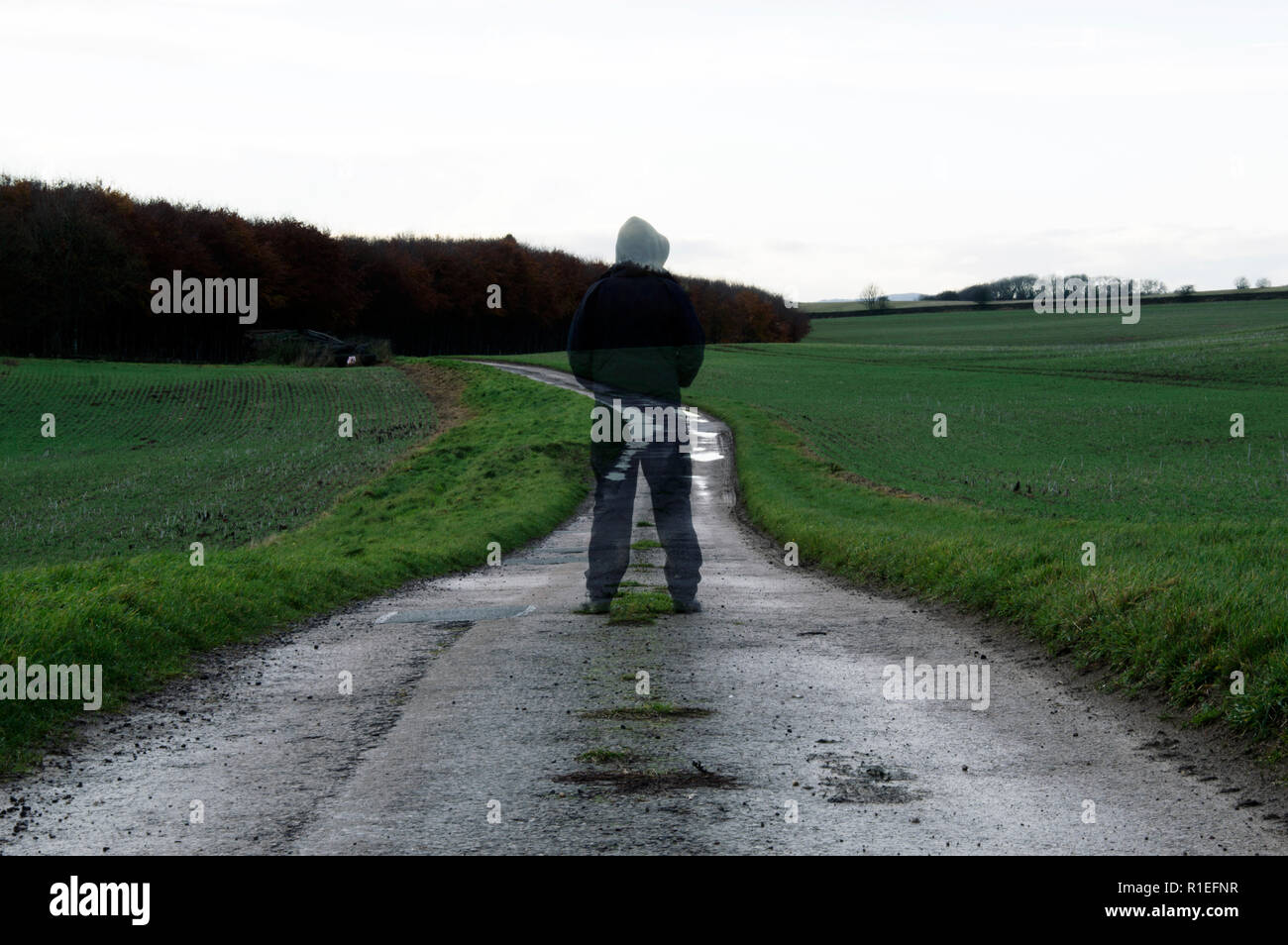 A ghostly, hooded transparent figure standing on a English country path on a winters day. With a muted edit Stock Photo