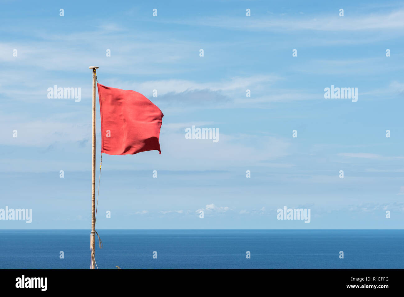 Red flag waving on a pole. Clouds and sea view background. Horizontal