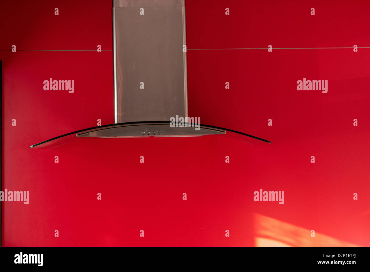 Kitchen rangehood made with chrome exhaust shaft and curved glass hood against a red background Stock Photo