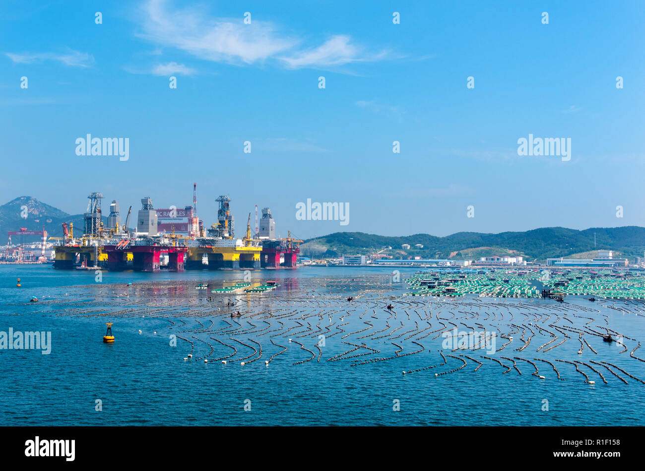 YANTAI, SHANDONG, CHINA - 21JUL2018: Semisubmersible rigs, owned by CIMC and subsidiaries compete for space with traditional fish farming. Stock Photo