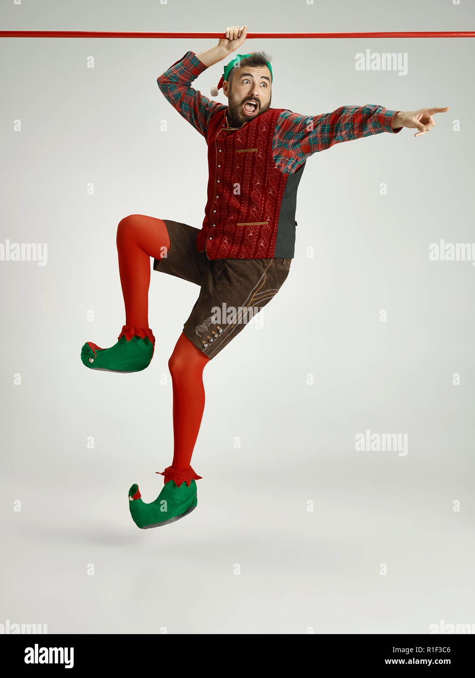 The happy smiling friendly man dressed like a funny gnome or elf hanging on an isolated gray studio background. The winter, holiday, christmas concept Stock Photo