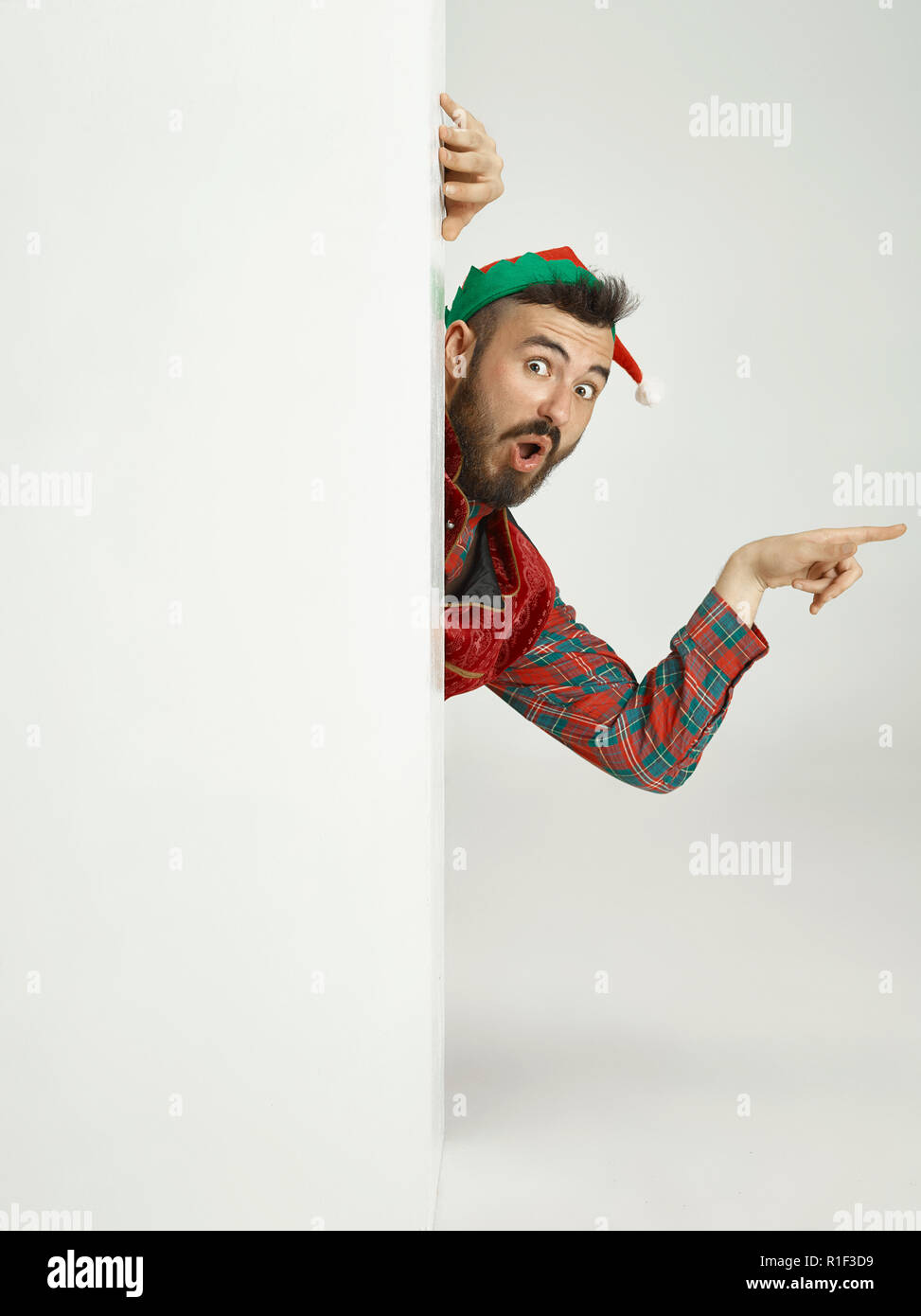 The happy smiling friendly man dressed like a funny gnome or elf posing on an isolated gray studio background. The winter, holiday, christmas concept Stock Photo