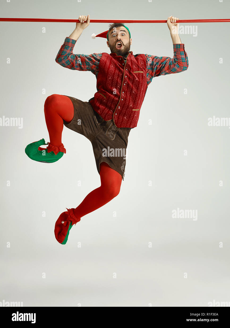 The happy smiling friendly man dressed like a funny gnome or elf hanging on an isolated gray studio background. The winter, holiday, christmas concept Stock Photo