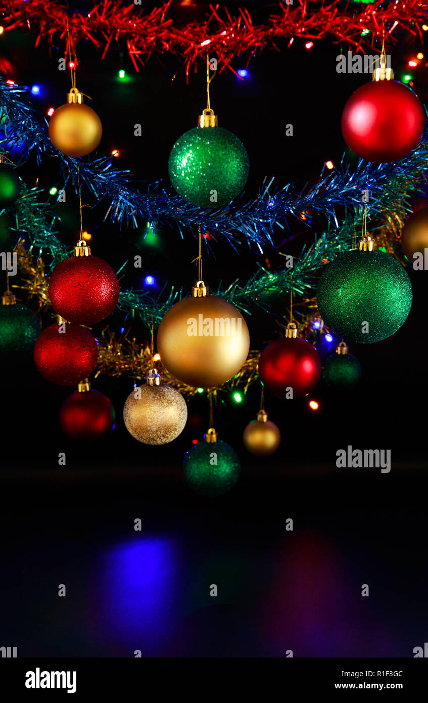 Close up of hanging Christmas decorations and Christmas/fairy lights against a black background. Stock Photo