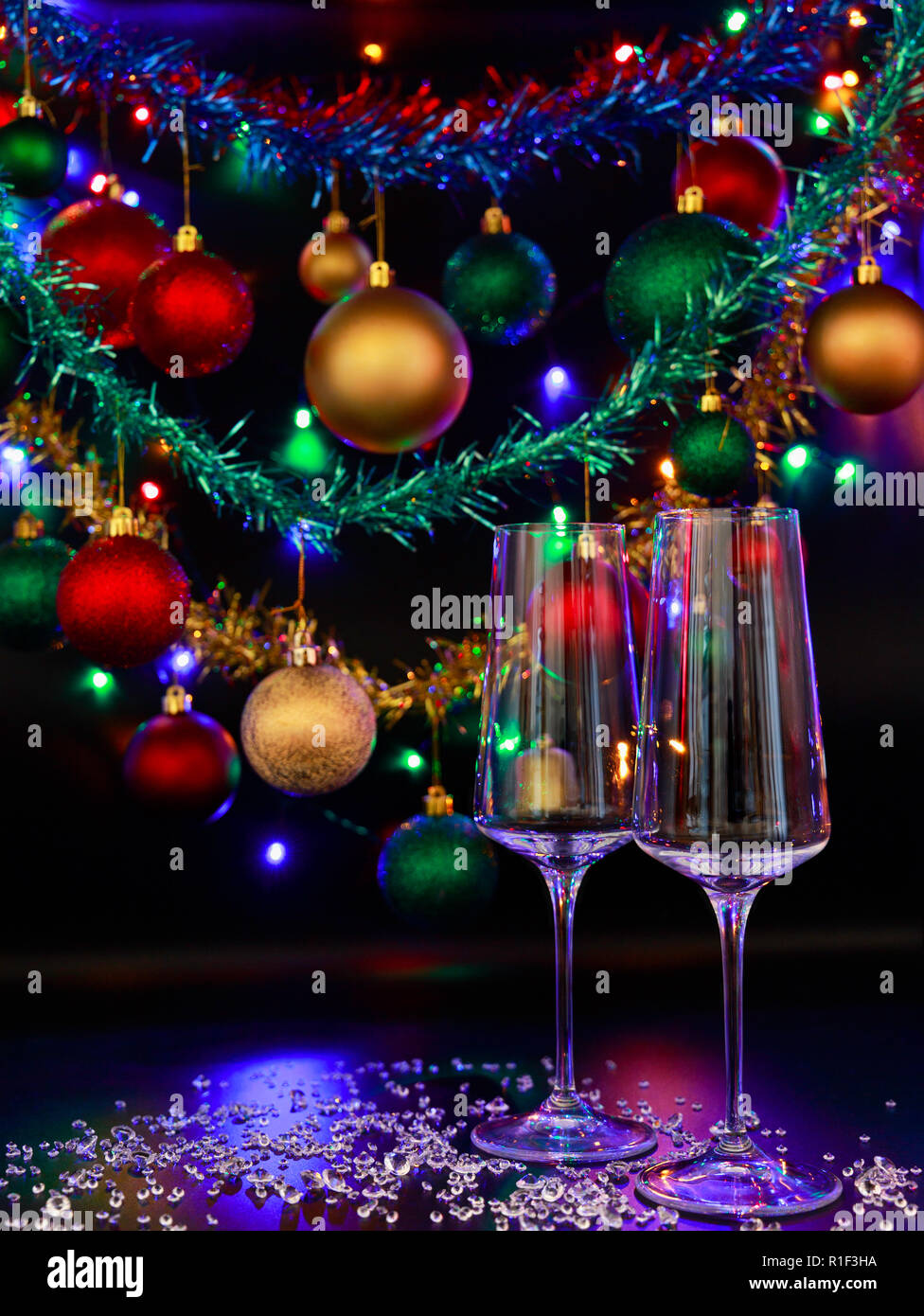 Two champagne glasses against a background of colorful Christmas decorations and Christmas lights. Stock Photo