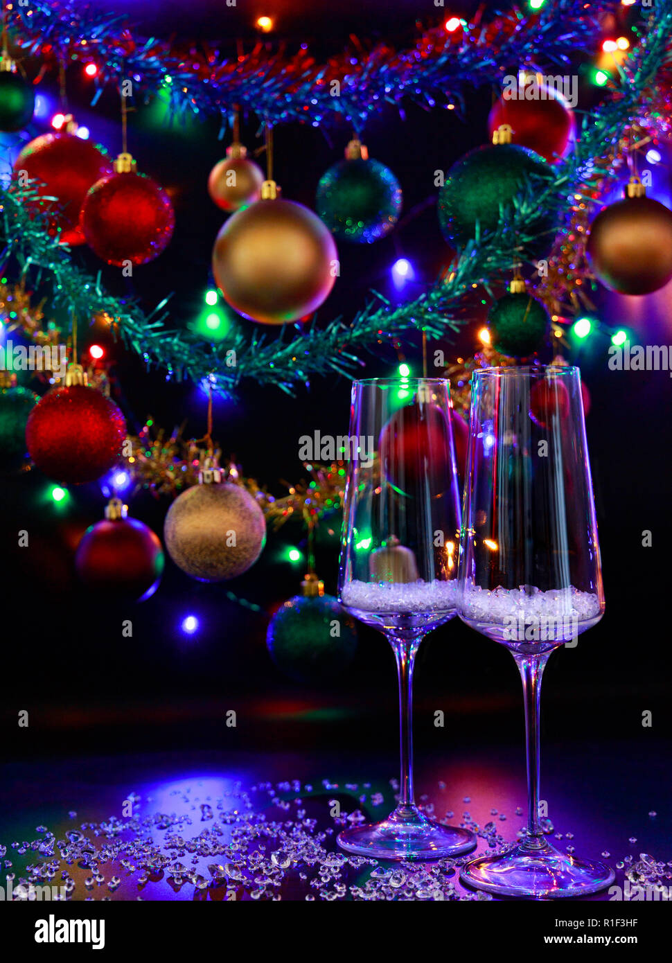 Two champagne glasses against a background of colorful Christmas decorations and Christmas lights. Stock Photo