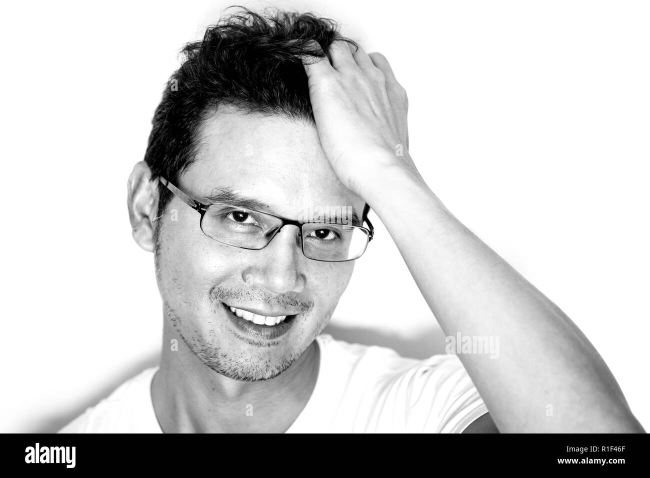 Portrait of handsome asian man with light beard wearing eyeglasses for near sighted smiling and touching his curly hair. Monotone black and white effe Stock Photo