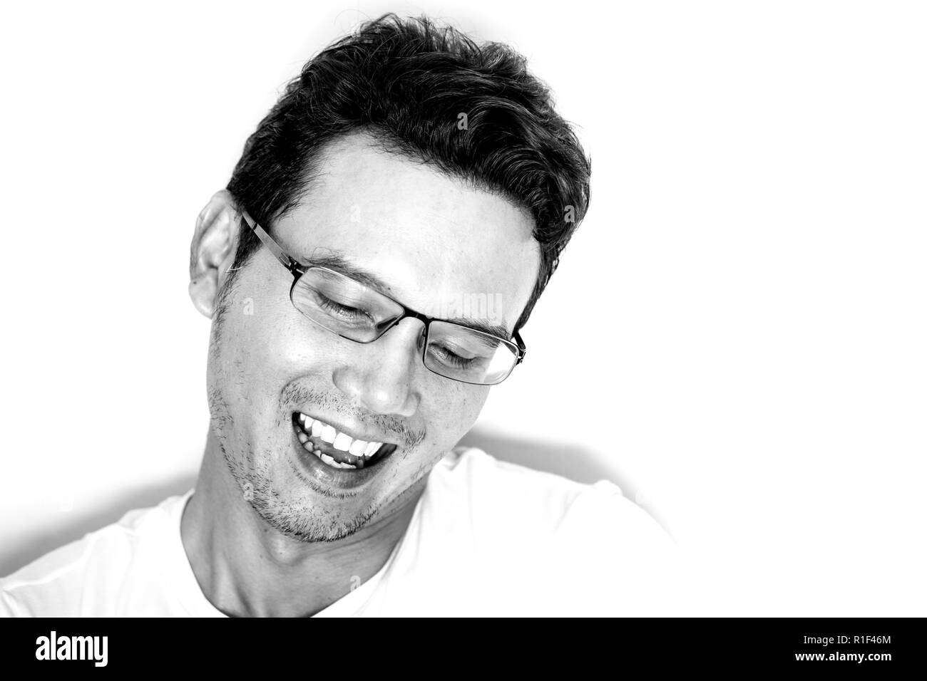 Handsome asian man with light beard and curly hair wearing eyeglasses for near sighted laughing and feeling funny. Monotone effect. Stock Photo