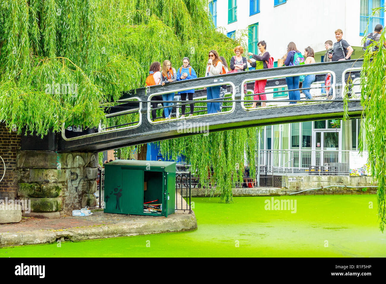 London, UK - September 1, 2018 - Tourists crossing the Camden Lock footbridge above Regents Canal covered by green duckweed Stock Photo
