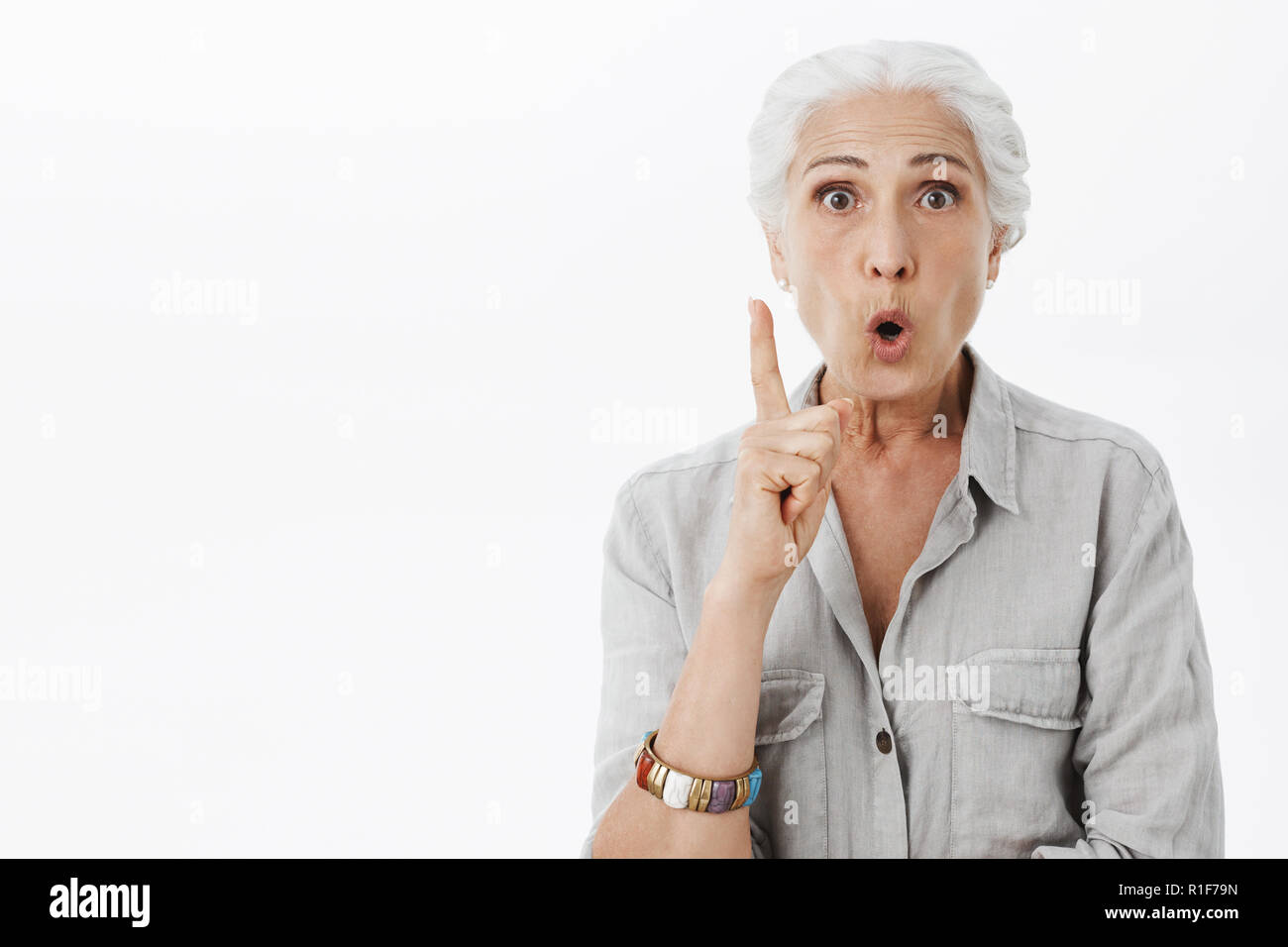 I got excellent advice for daughter. Portrait of excited and enthusiastic creative senior woman with white hair folding lips raising index finger in eureka gesture while having idea adding suggestion Stock Photo