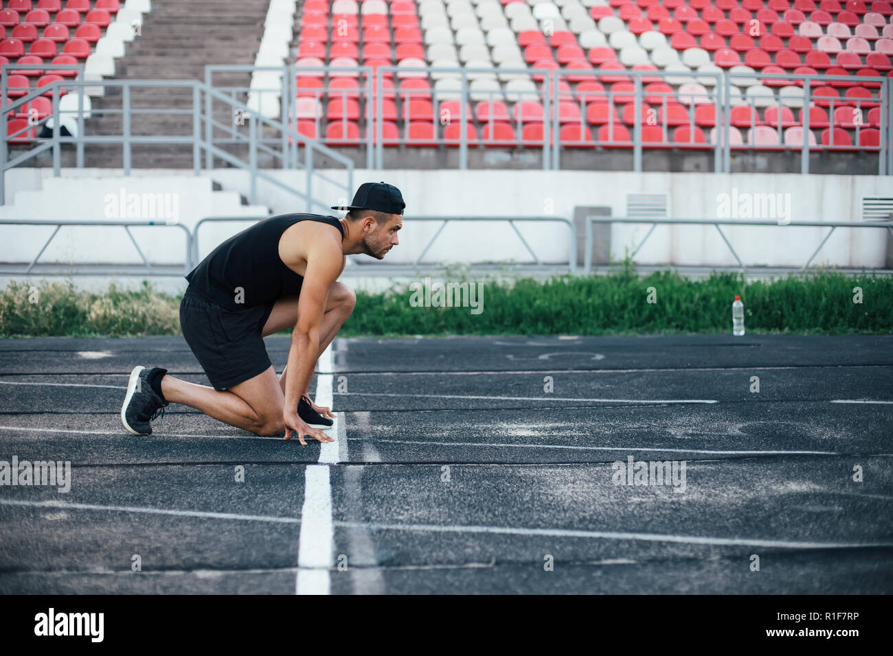 Athlete man in running start pose on the running track in stadium Stock Photo