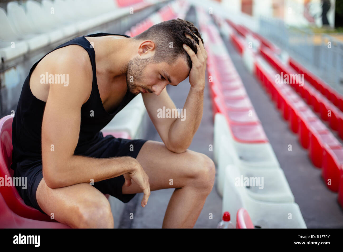 Depressed athlete man sitting head in hands on stadium seats, stress