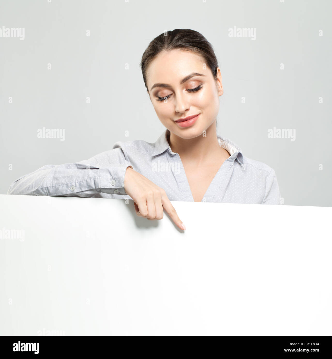 Friendly young woman pointing and holding white empty signboard paper background. Happy student girl, business and education concept Stock Photo
