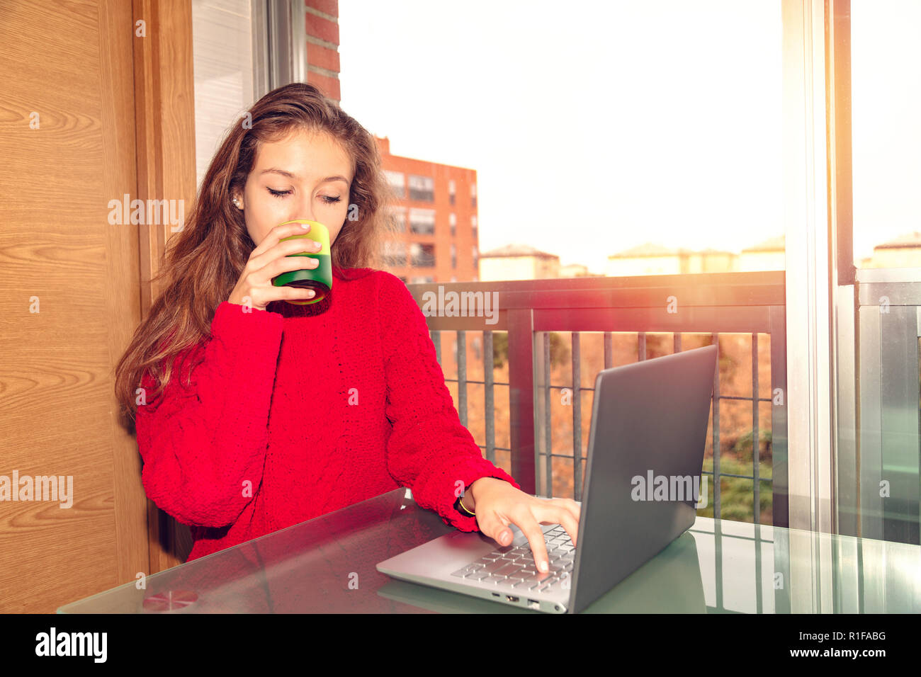 Girl freelancer working with laptop and drinking beverage from glass Stock Photo
