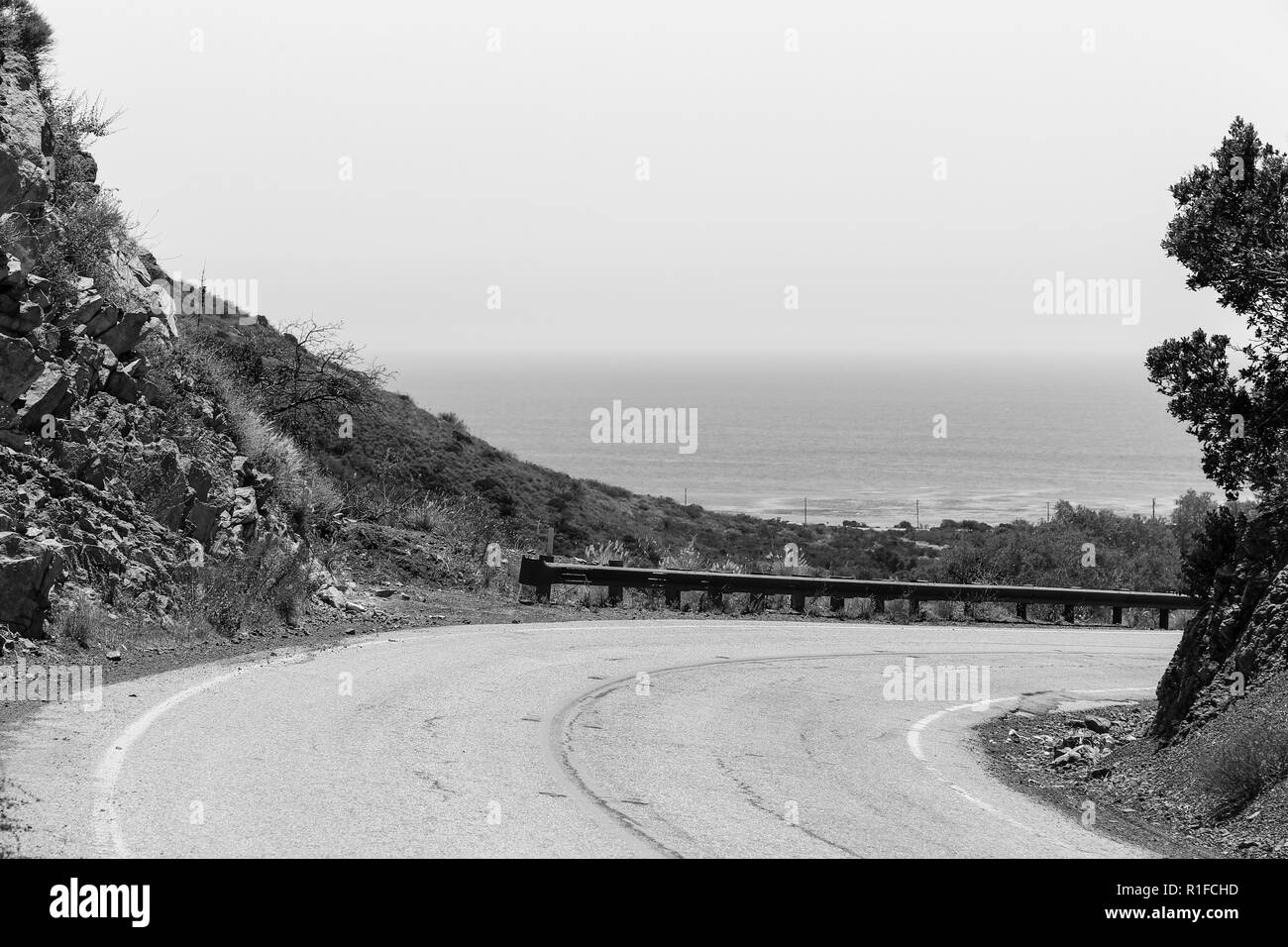 A curve on the Mulholland Highway in the Malibu Hills. In the background is the Pacific Ocean. Captured in black and white. Stock Photo