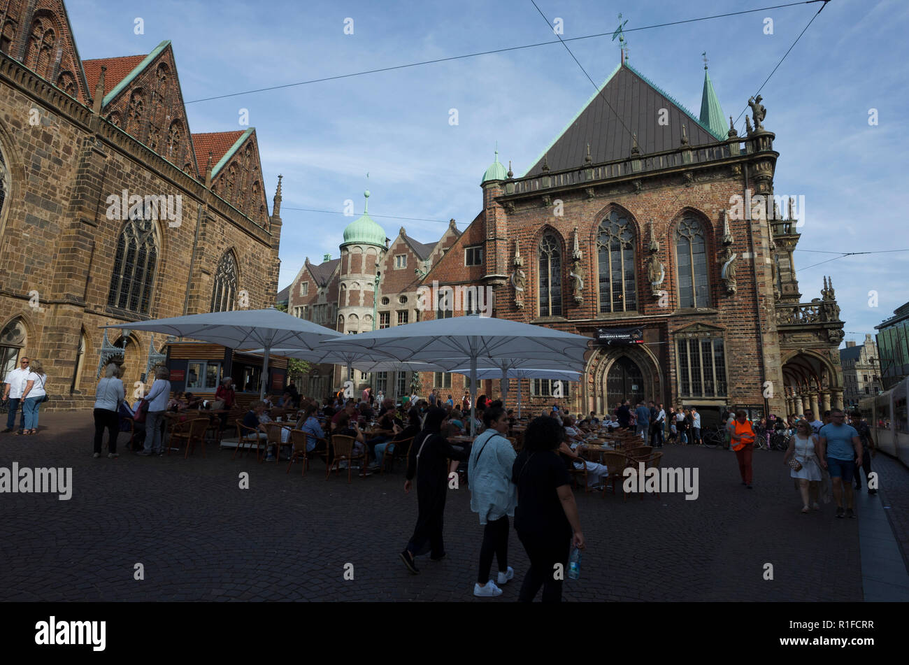 Marktplatz, Bremen. Deutschland Germany.  A scene looking across the market square looking upon an outside area reserved for serving refreshments for drinks and light meals.  Many people are enjoying refreshments while others walk by.  Large parasols protect them from the elements whether that's rain or strong sunshine although it's currently under shade. Stock Photo