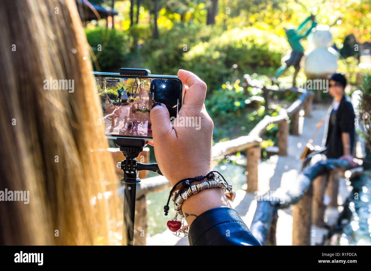 Over the shoulder shot as a lady takes a photograph of her friend using an iPhone smartphone. Stock Photo