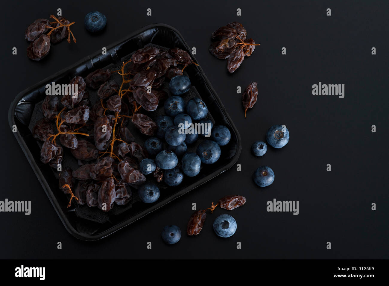 Bunch of dried sultanas and blue berries on a tray isolated on black background Stock Photo