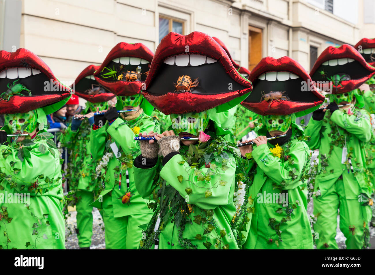 Basel carnival. Steinenberg, Basel, Switzerland - February 21st, 2018. Close-up of a carnival group in bright green costumes with red mouths on their  Stock Photo