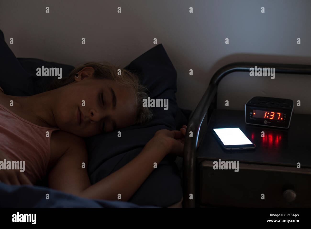 Young girl in bed late at night sleeping with her mobile phone on her night stand. Stock Photo