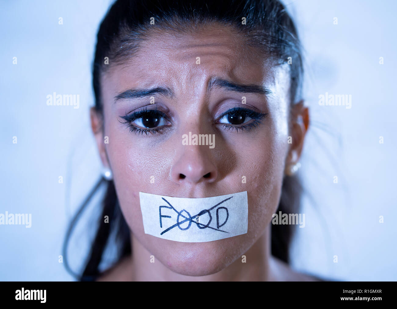Close up portrait of young attractive latin woman with mouth sealed on stick tape with text no food in diet Anorexia eating disorder concept. Stock Photo