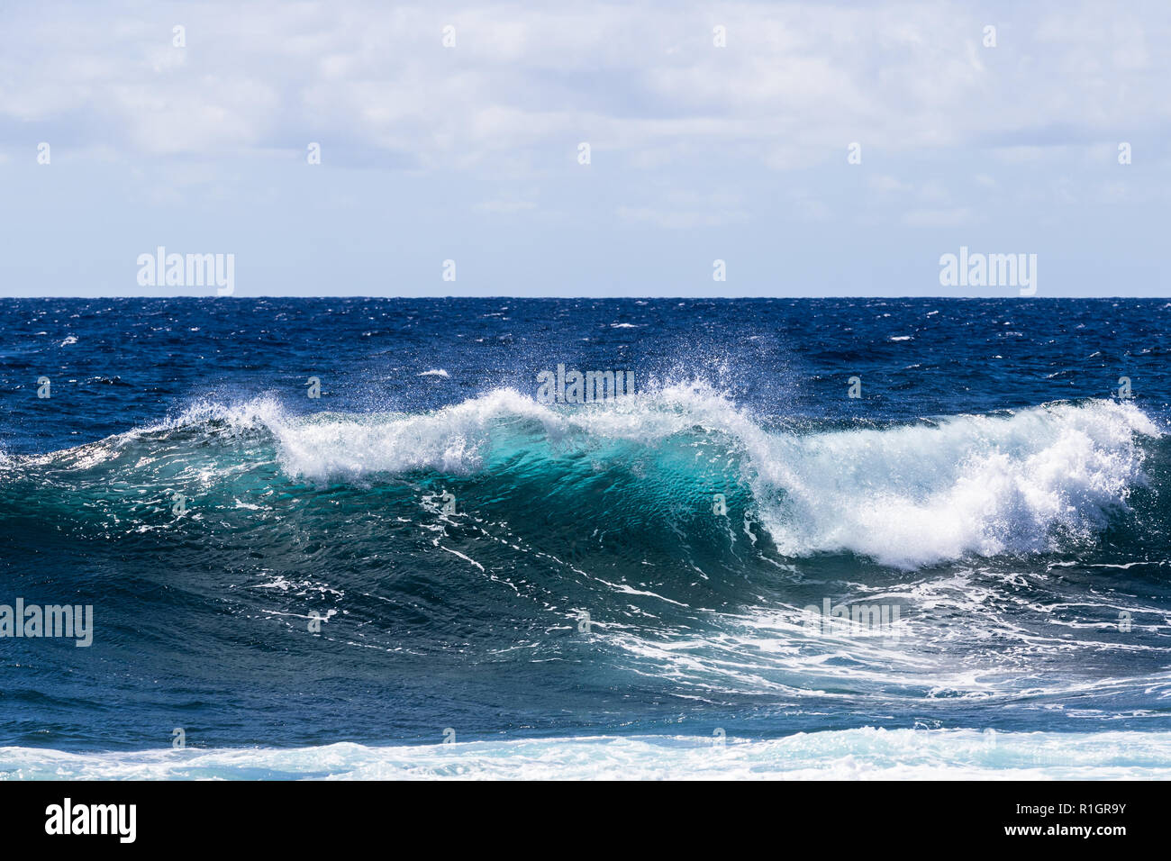 Wave breaking near shore on South Point, on Hawaii's Big Island. Foam on top of wave's clear blue-green water; Pacific ocean in the background. Stock Photo