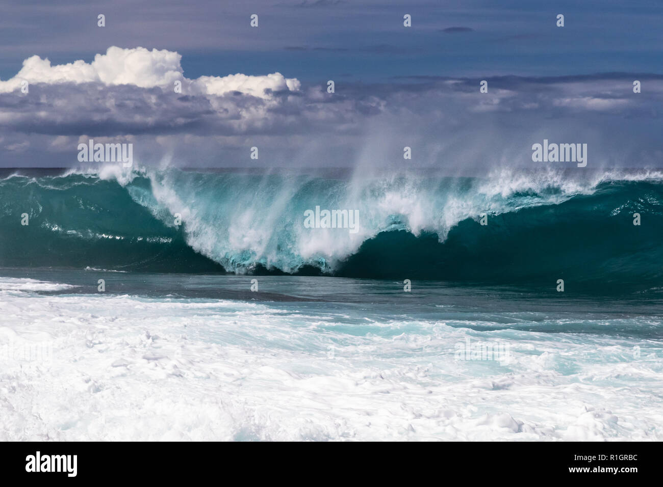 Wave curling on Hawaiian beach, about to crash on the water below. Spray flyng back on wave's top. South Point. White sea spray thrown into the air. Stock Photo