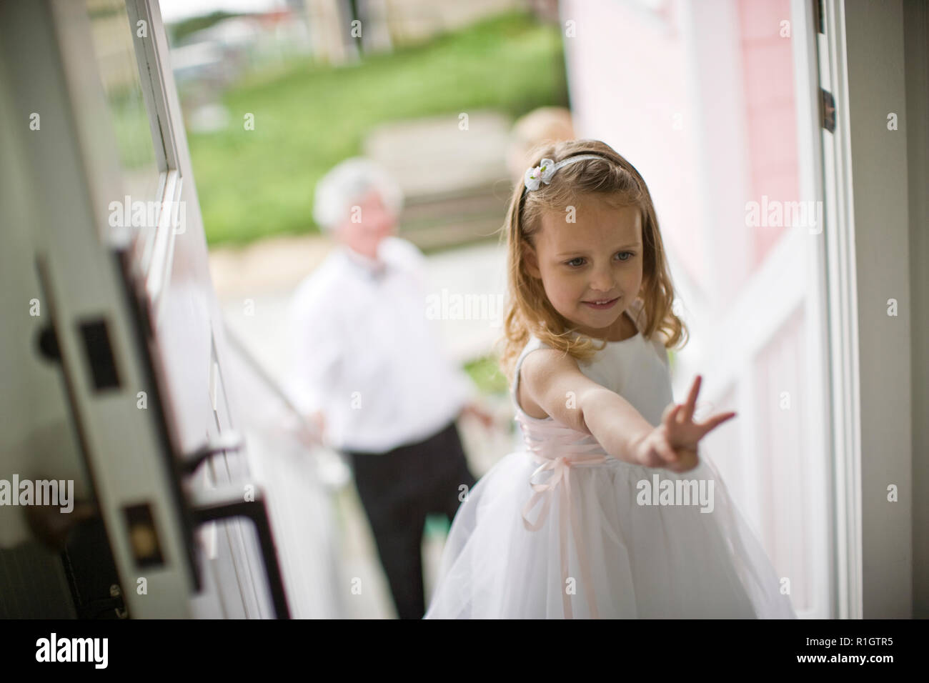 Young girl dressed as a flowergirl holding up three fingers while standing at the front door of her home. Stock Photo