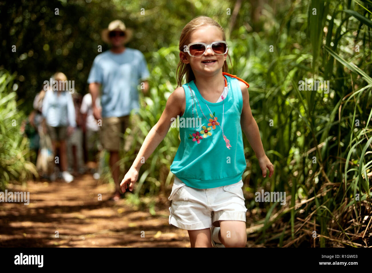 Little girl with her family in the background, hiking through cultivated vegetation in a tropical climate. Stock Photo