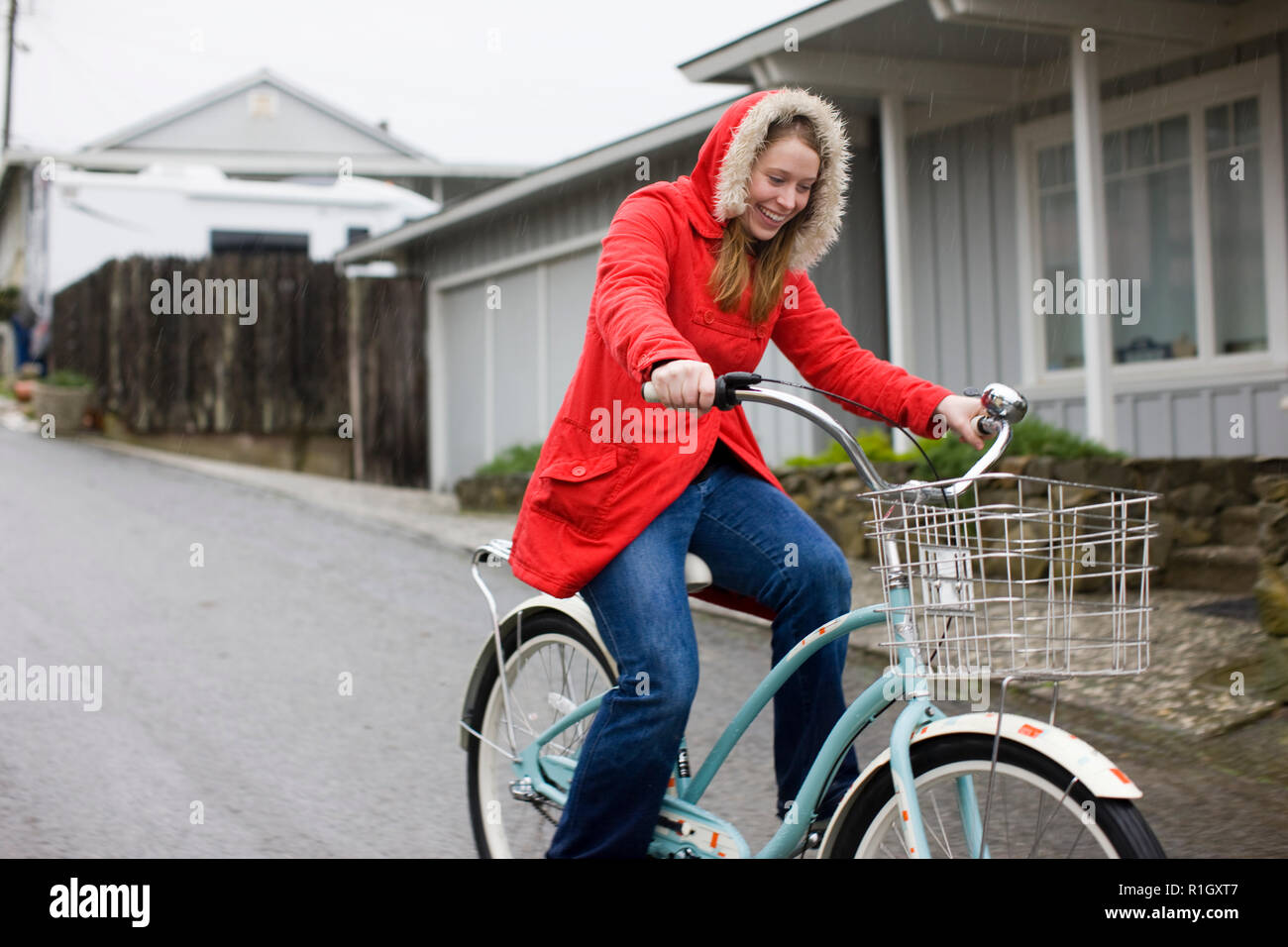 Smiling young woman riding a retro bicycle on an empty suburban street. Stock Photo