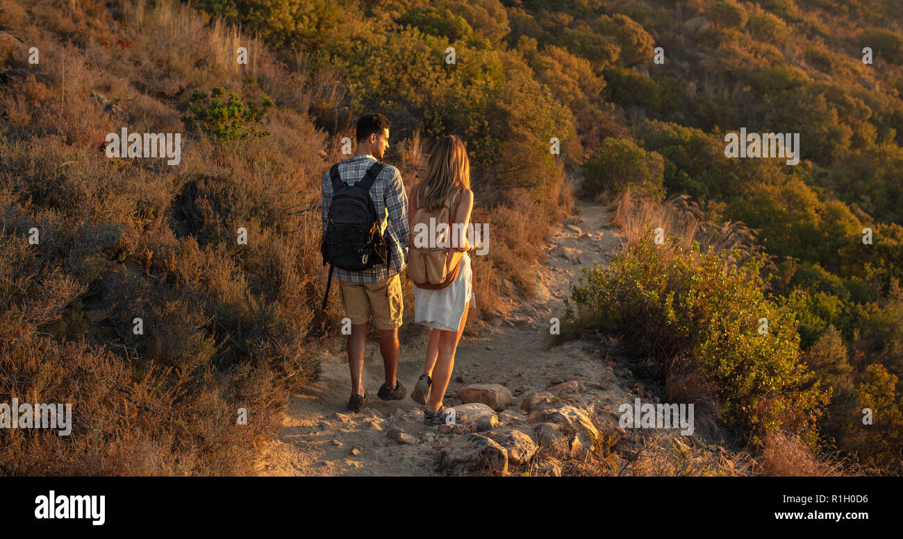Rear view of man and woman hikers trekking a rocky path at hill side. Hiker couple exploring nature walking through mountain trail. Stock Photo