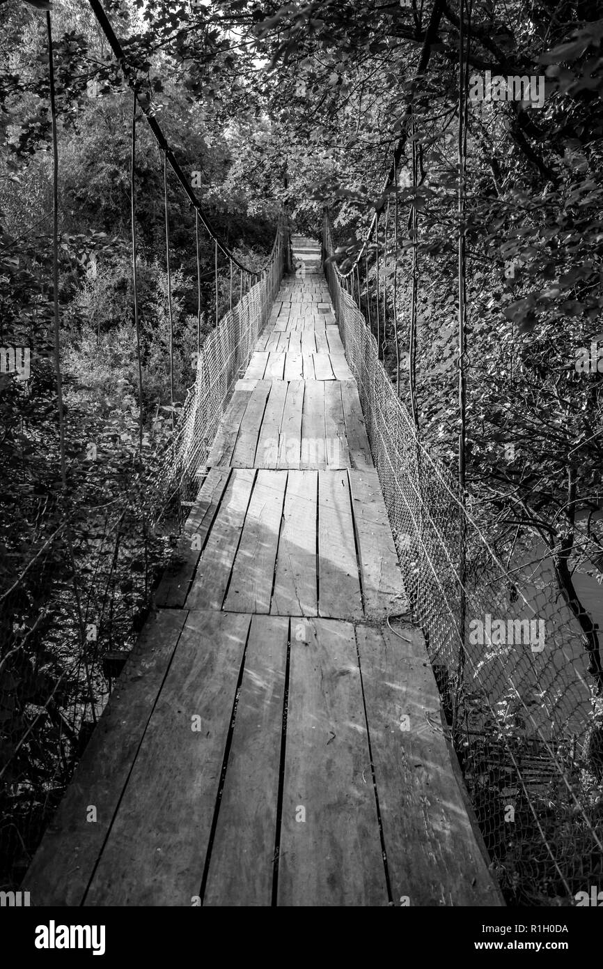 Old suspension footbridge covered with wooden planks in the village of Debnevo, Stara Planina mountain, Bulgaria. Black and white picture, nice perspe Stock Photo