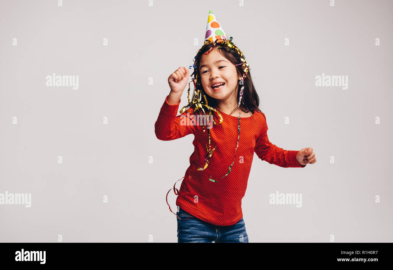 Portrait of a happy kid dancing wearing a party cap and ribbons on head. Cheerful asian kid having fun dancing. Stock Photo