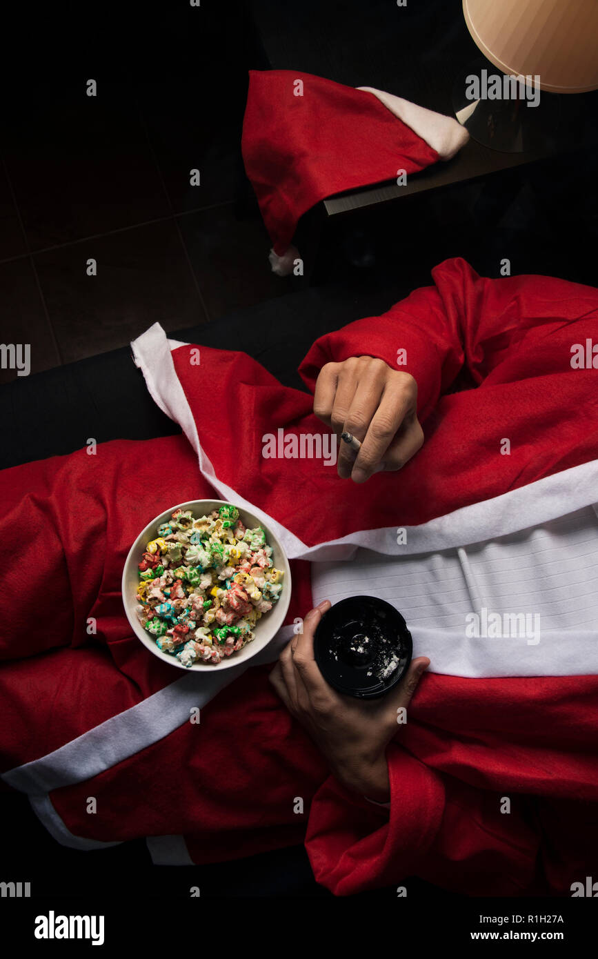 high angle view of a young man wearing a santa suit smoking a cigarette and eating popcorn in bed Stock Photo