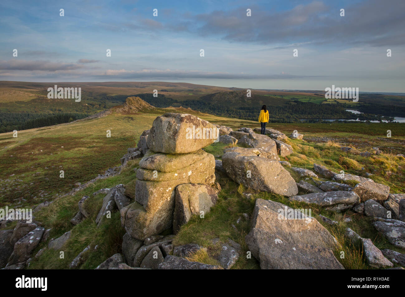 Woam in bright yelloe top standing on Sharpitor rocks looking towards Leather tor at sunset Stock Photo