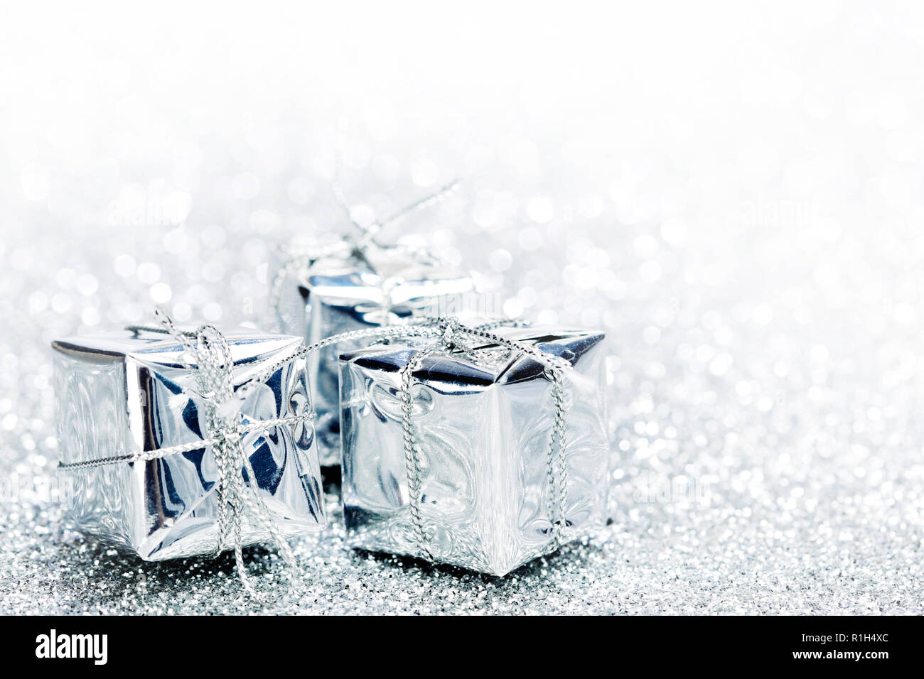 Decorative silver boxes with holiday gifts on shiny glitter background