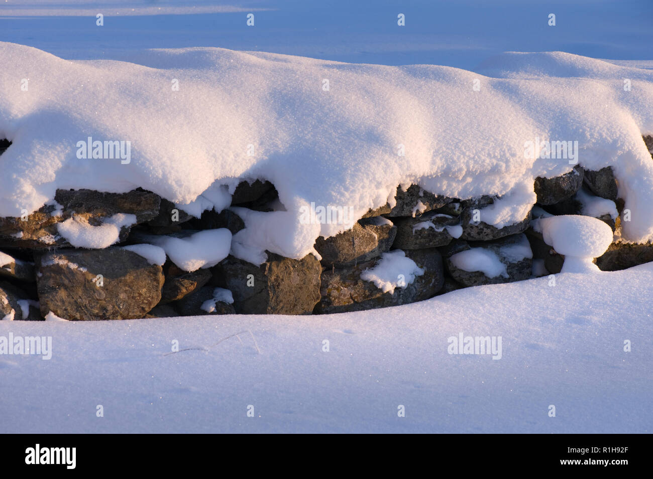 Snow covered old stone wall lit by a low angle sun. Stock Photo