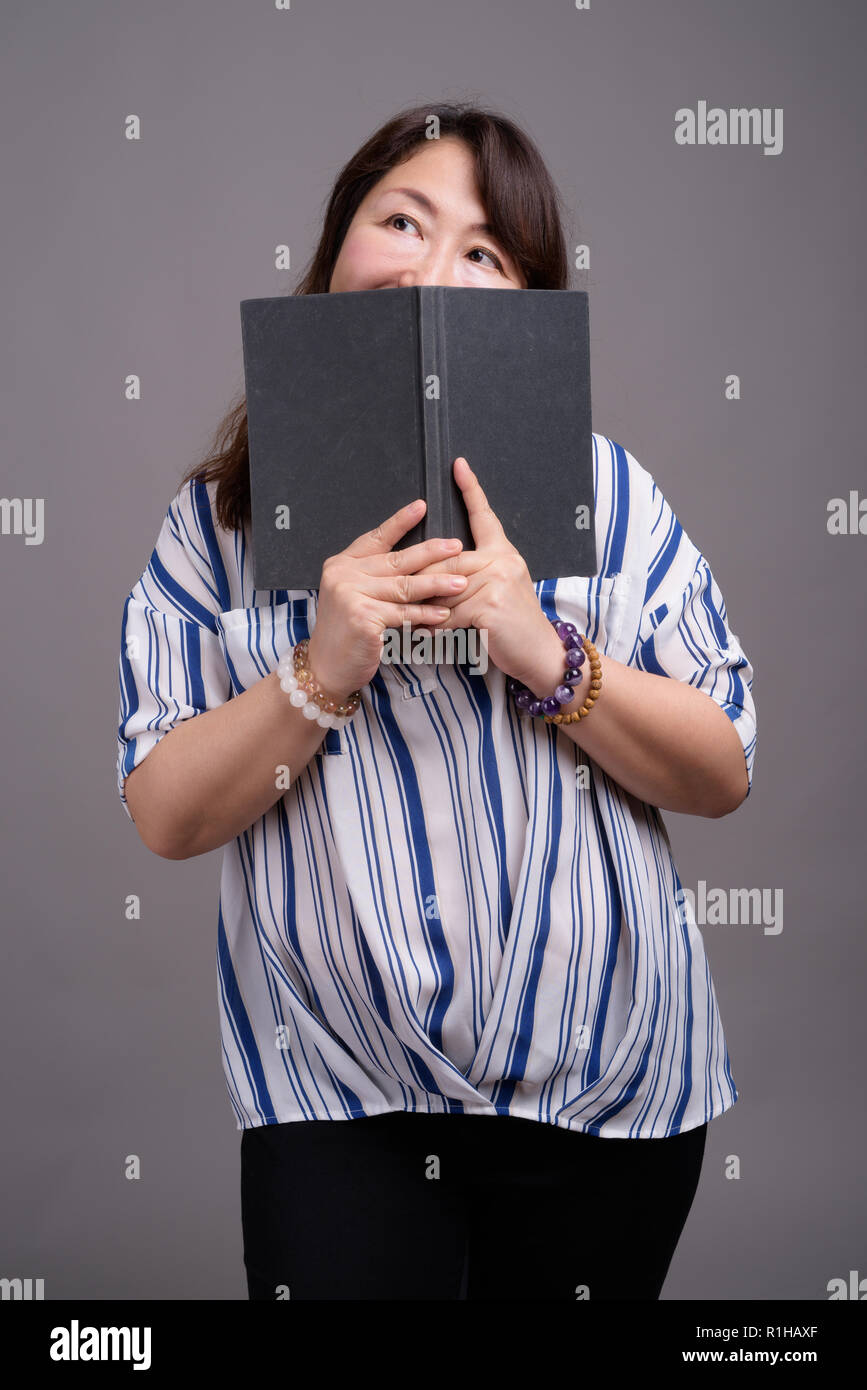 Mature beautiful Asian businesswoman hiding behind book Stock Photo