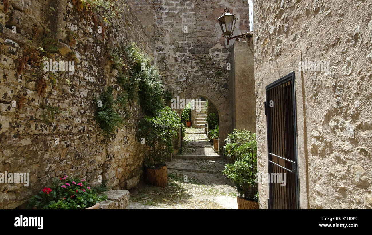 Narrow path between high stone walls and stone houses houses in Italy in Sicily Stock Photo