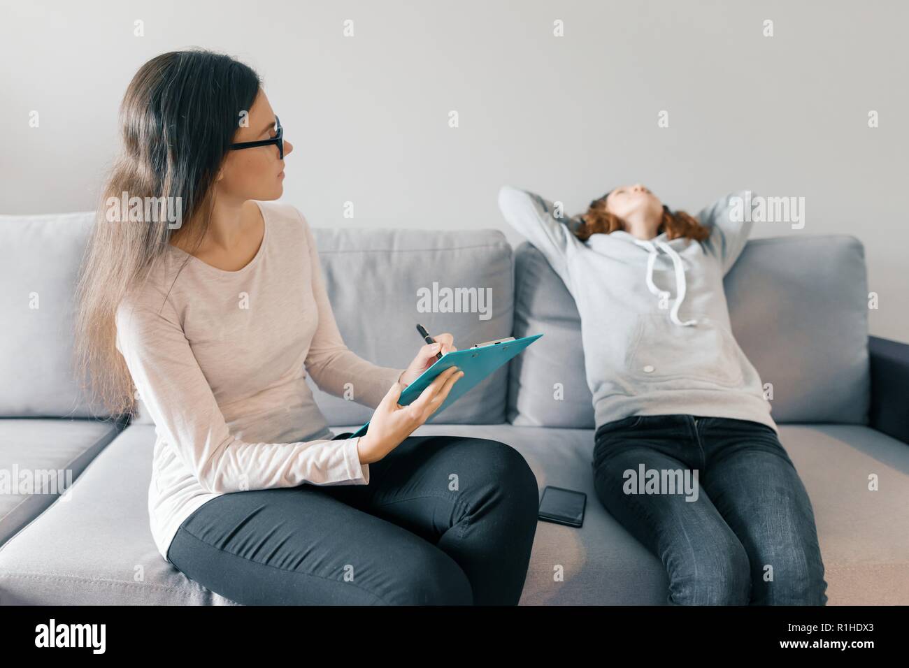 Professional child psychologist talking with teenager girl in office, girl sitting on the sofa. Stock Photo