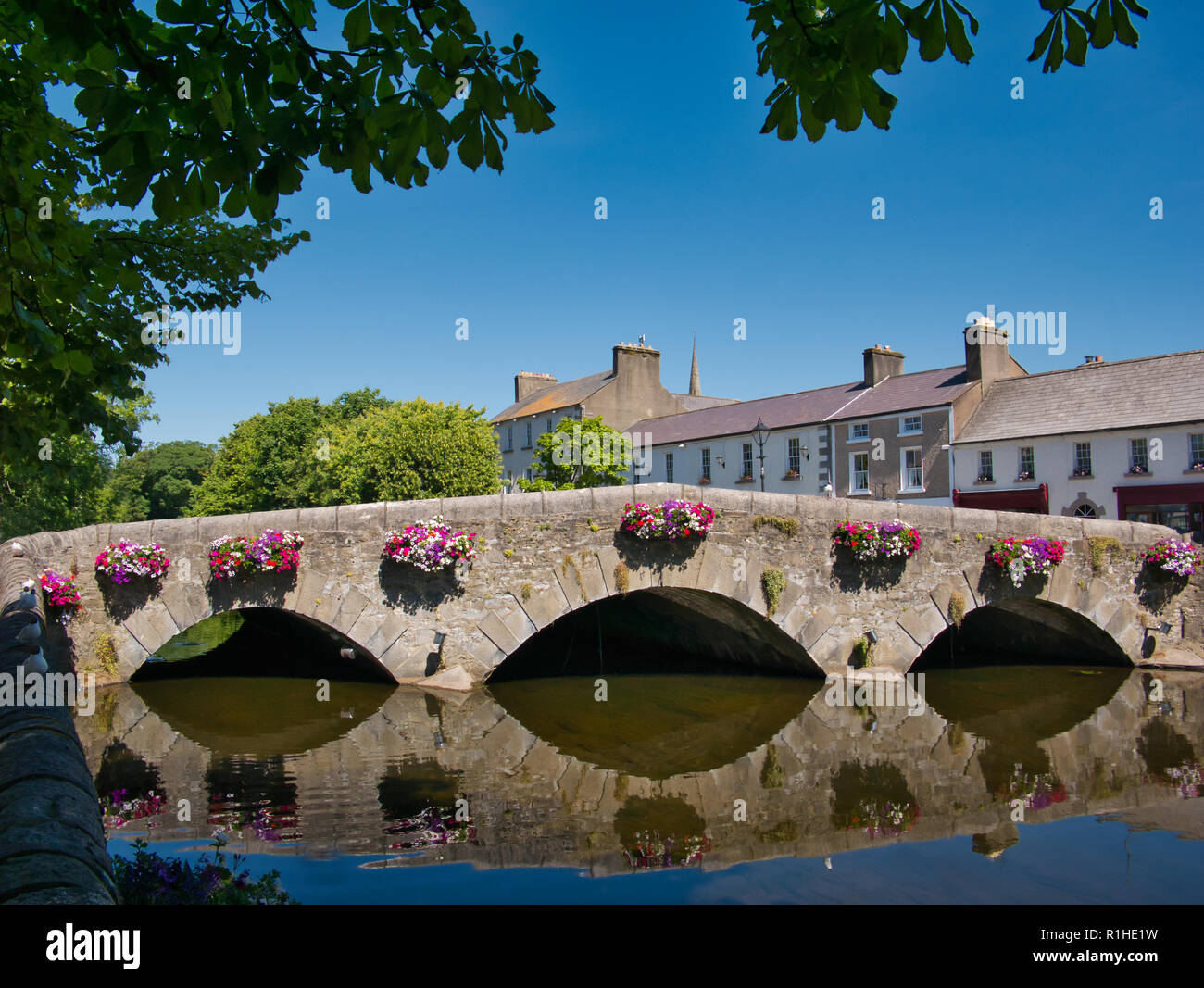 An old bridge with flowers is reflected in the water in front of a row of houses in Westport. Stock Photo