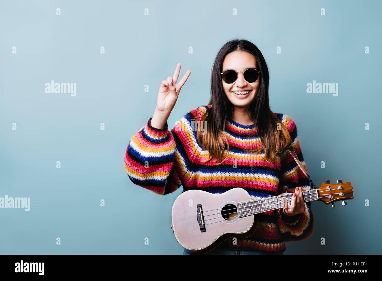 Young girl with a ukulele and giving peace sign with hand Stock Photo