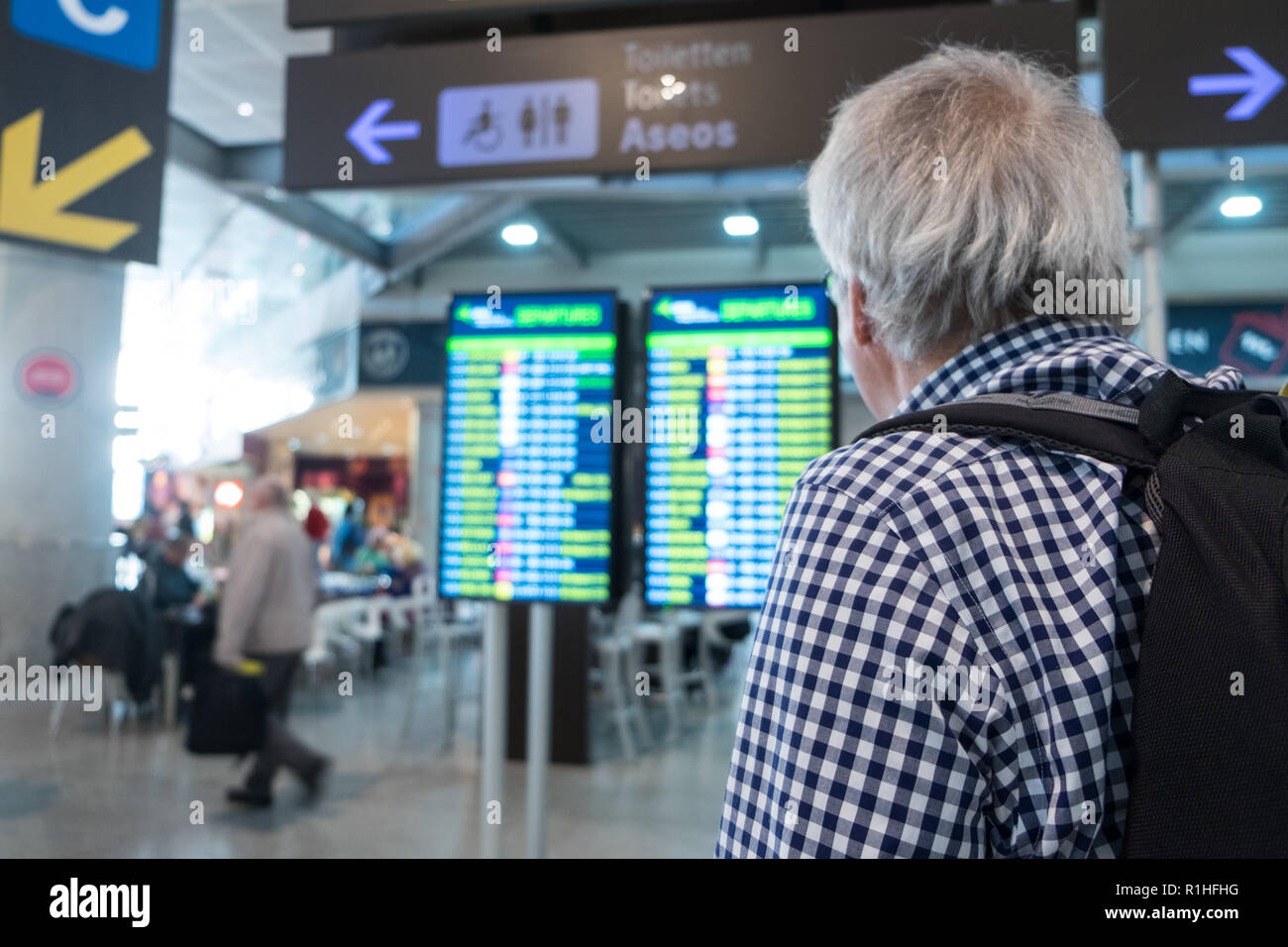 Senior male looking a airport departures board at departure terminal, waiting for plane, international signs and directions Stock Photo
