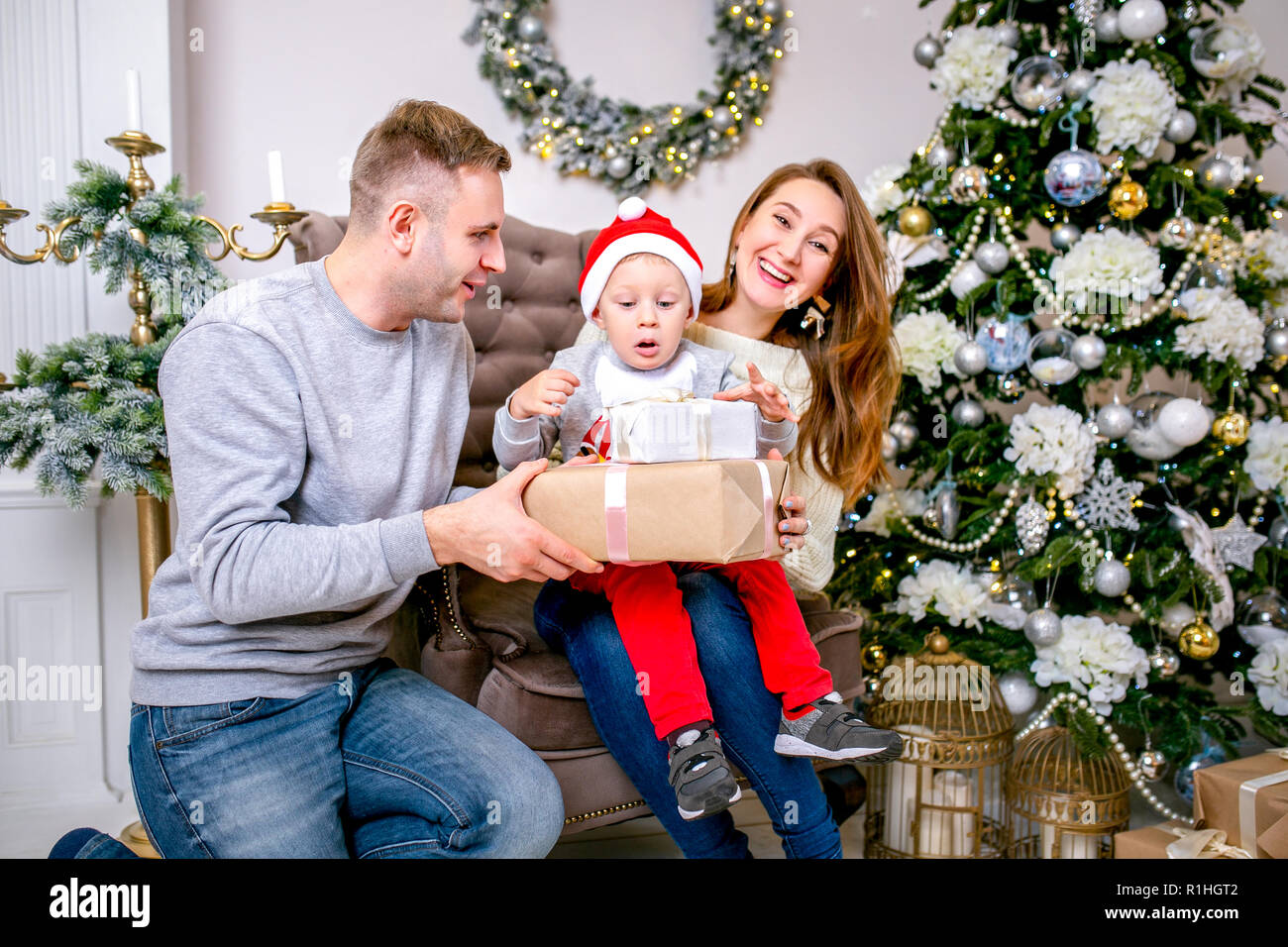 Happy family, father, mother and son, in the morning in living room decorated for Christmas. They open presents and have fun. New Year's and Christmas theme. Holiday mood Stock Photo